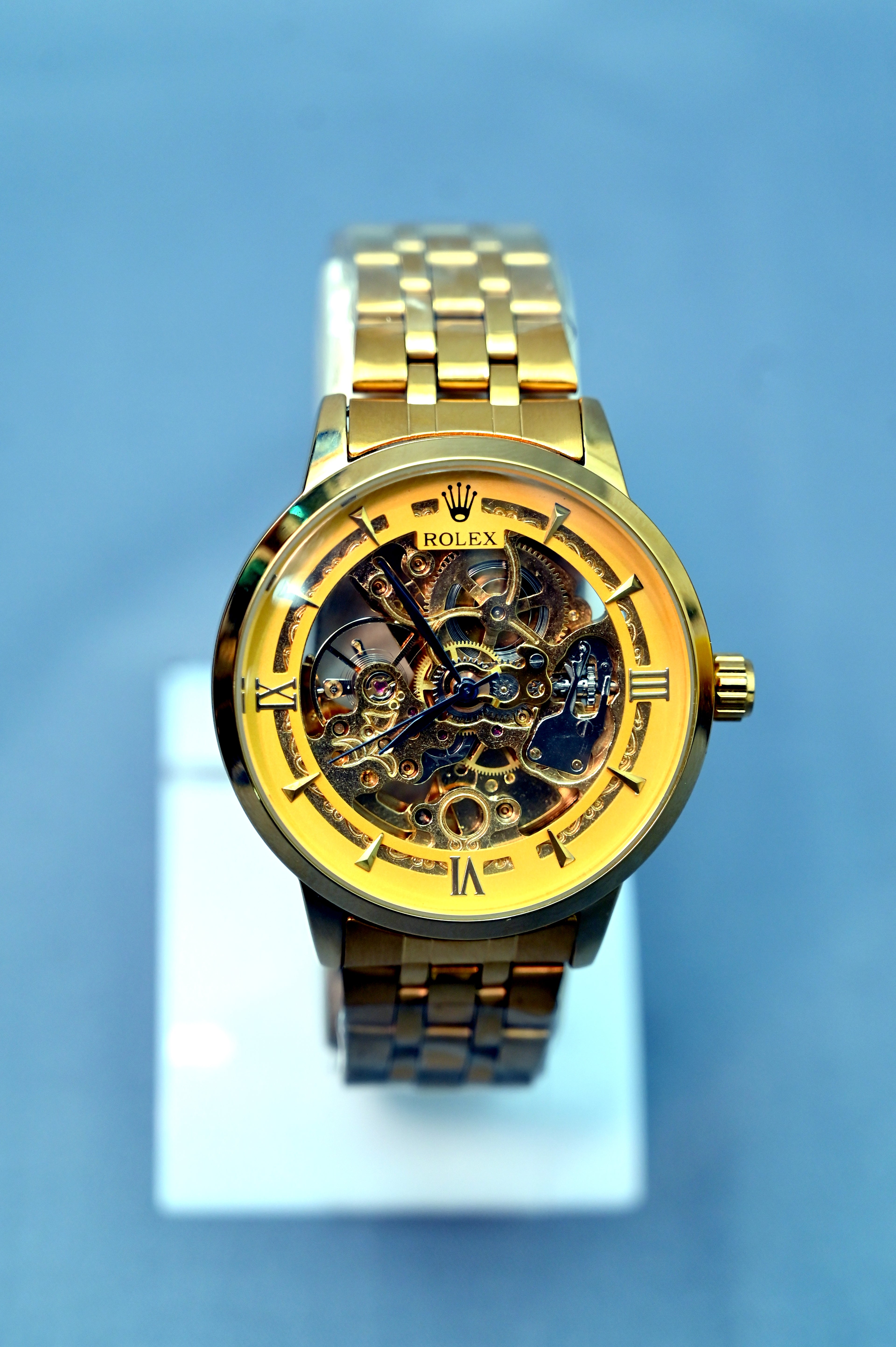 Gold Rolex watch on a white stand with a blue gradient background